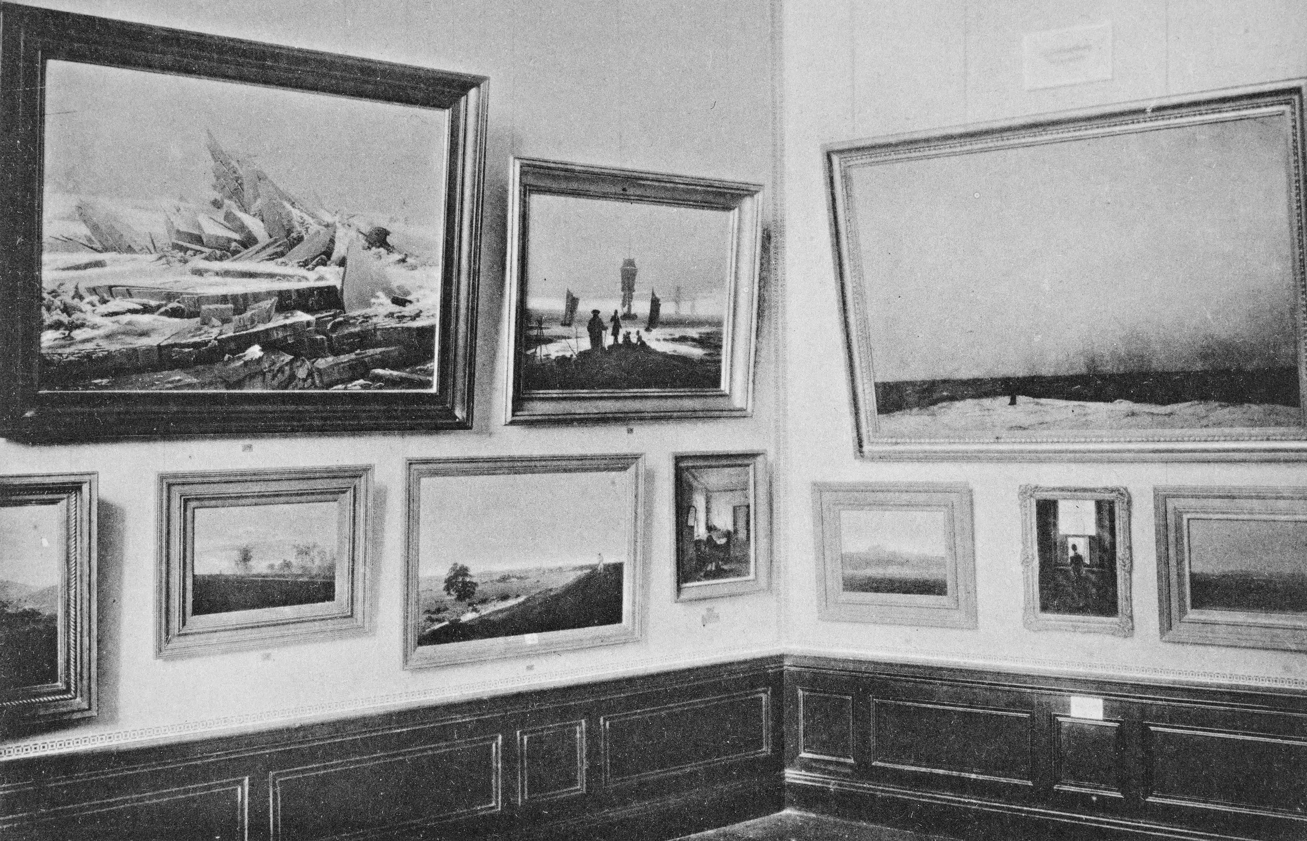 Ansicht eines Raumes mit Werken von Caspar David Friedrich auf der Deutschen Jahrhundertausstellung 1906. Hängung in zweireihig übereinander auf weißen Wänden. Zu erkennen sind unter anderen die Gemälde „Das Eismeer“, „Lebensstufen“ und „Mönch am Meer“. 